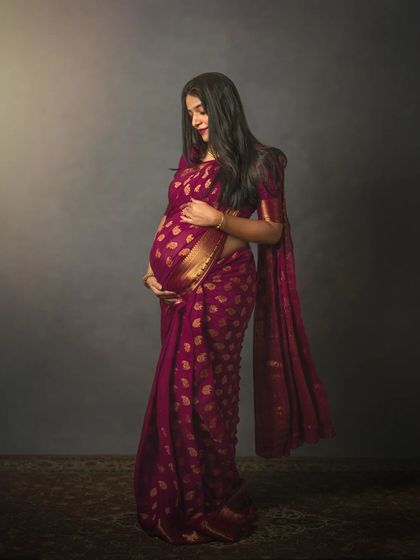 A duplicate of ID 69, this full-length studio portrait of an expecting mother in a gorgeous magenta saree showcases her graceful silhouette. The simple, dark backdrop makes the rich color and gold details of the fabric stand out.