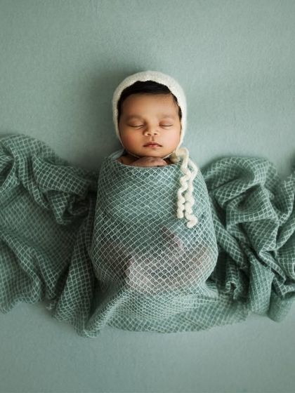 Welcoming the tiniest miracles with a touch of artistry. This baby is wrapped in a soft green swaddle, with the fabric fanned out like angel wings.