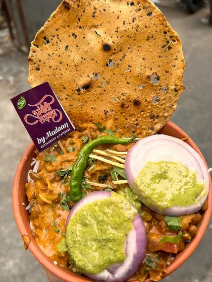 A close-up of our delicious Rajma Chawal served in an earthen bowl, topped with fresh onions, green chutney, and a crispy papad. It's a simple yet incredibly satisfying meal.