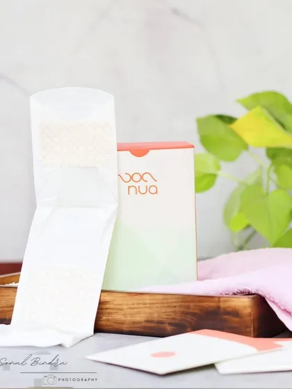 A clean and minimal shot focusing on the soft, skin-friendly design of a sanitary pad. The natural light and simple props create a fresh, modern, and relatable visual for a feminine hygiene brand.