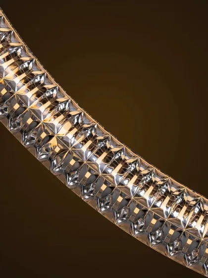 A macro shot of the Luminora pendant's surface, revealing the detailed texture and torsion effect that catches the light. This emphasizes the craftsmanship and ornamental quality of the design.