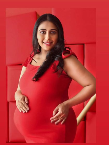 A bright and joyful portrait of a mother-to-be in a simple red dress. Her happy expression and the vibrant red background create an image that radiates warmth and excitement.
