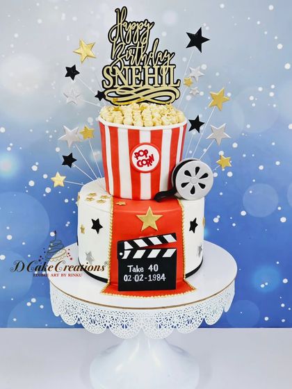 A clean studio shot of the two-tier Bollywood cake, showing the edible popcorn, film reel, and personalized clapperboard.