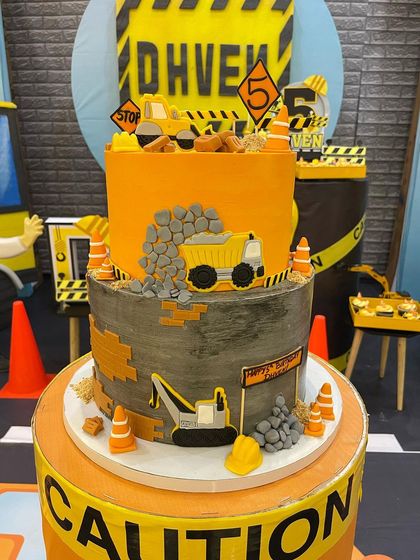 A full view of my popular two-tier construction cake, ready for a 5th birthday party. The design includes a dump truck spilling edible rocks, an excavator, and caution signs for a busy building site.