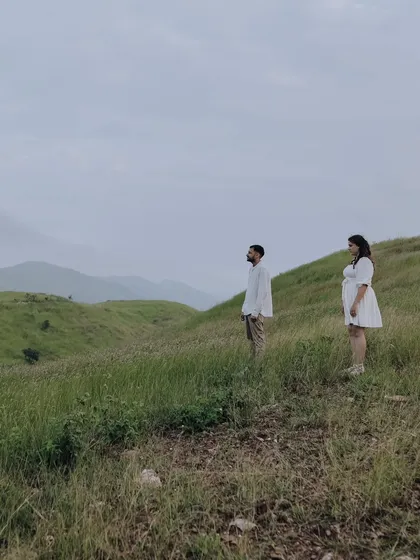A wide, atmospheric shot of the couple looking out over a vast green valley, creating a sense of contemplation and shared dreams.