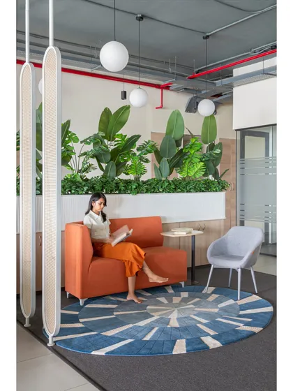 A quiet moment in the breakout zone. The space is designed to be a versatile hub, with a mix of textures from the patterned rug to the fluted planter details, all surrounded by calming greenery.