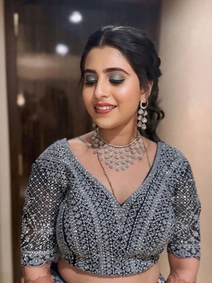 A client ready for a wedding reception in a beautiful grey lehenga. Her makeup features a smoky eye and a soft pink lip, paired with a romantic, loosely braided ponytail.
