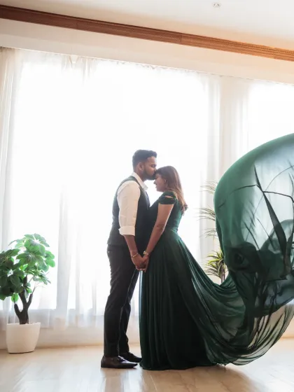 A powerful silhouette of the couple against a brightly lit window. The groom's gentle kiss on her forehead and the motion of her flowing green dress create a moment of pure cinematic romance.