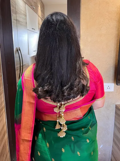 A simple open hairstyle with soft curls at the ends. The hair is neatly pinned back to show off the beautiful blouse latkans.