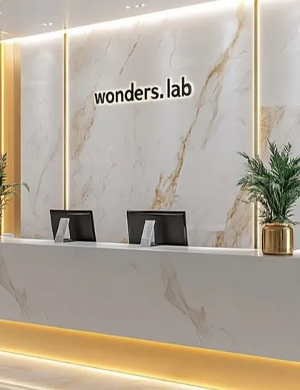 We designed this high-end reception area for "wonders.lab" to be impressive and professional. The space features a custom desk and a stunning floor-to-ceiling marble accent wall with gold-veining, complemented by warm under-desk lighting and elegant brass planters.