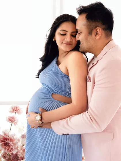 A tender moment between an expecting couple, set against a beautiful floral arrangement. The soft colors and gentle embrace highlight the love and anticipation.