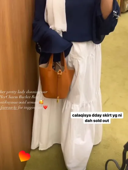 A customer showing off her HerCharm Bucket Bag in LV brown. It's a great everyday bag that adds a pop of colour to a simple white skirt and navy top.