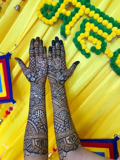 A beautiful full-arm mehandi with a mix of traditional motifs, including peacocks and geometric patterns, set against a festive yellow background.