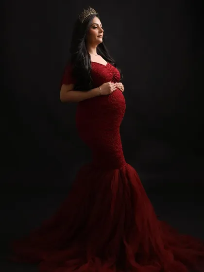 A profile of a queen. This elegant pose showcases the beautiful silhouette of the baby bump and the intricate details of the red lace gown.
