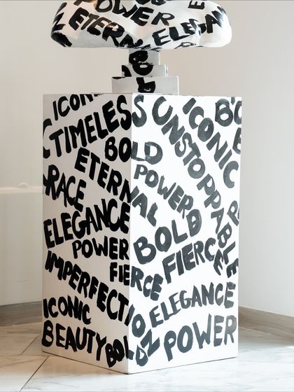 The base of the "Medusa: The Eternal Icon" sculpture, covered in empowering words like "Timeless," "Bold," and "Power."