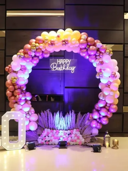 A circular balloon arch in shades of pink, peach, and gold creates a stunning photo spot for a 40th birthday party, complete with a neon sign and marquee numbers.