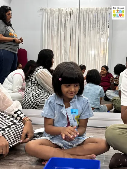 A child sits focused on a sensory play activity, surrounded by other children and parents. This captures the calm, community-focused environment of our club.