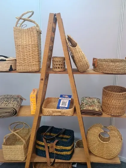 A display of our various woven products on a wooden ladder shelf at a market or fair. This image shows a range of our baskets, bags, and mats, highlighting the diversity of our handcrafted, sustainable goods.