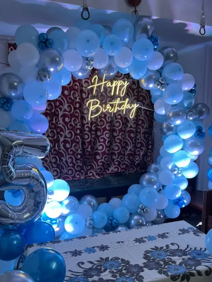 A beautiful blue and silver balloon ring for a Frozen themed 5th birthday party. The setup includes a "Happy Birthday" neon sign and a large number '5' foil balloon.