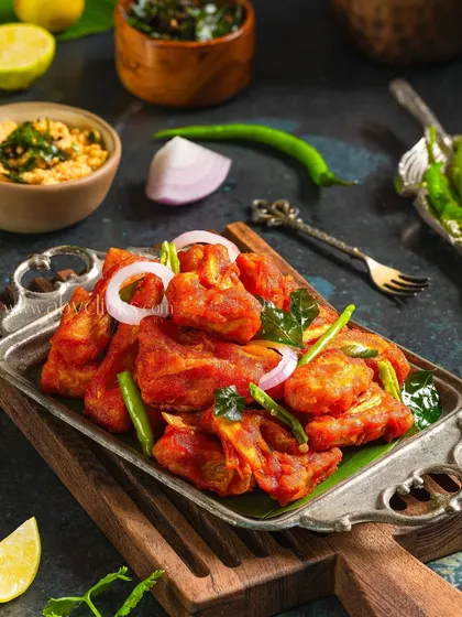 Chicken 65, a spicy fried chicken appetizer. The vibrant red color and fresh garnishes make it look irresistible.