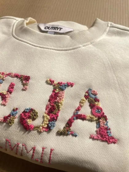 A close-up of the magic. I love filling initials with tiny, colorful flowers. Each petal and leaf is stitched by hand, making every floral letter a unique piece of art, like this 'TEJA' sweatshirt.