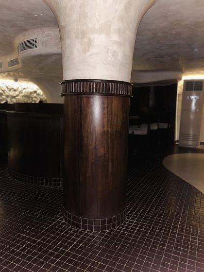 The dark, small-format grid tile flooring at "Call me ten" provides a continuous, textured base that unifies the space. It contrasts with the smooth, lime-washed pillar, highlighting the project's focus on material interplay.