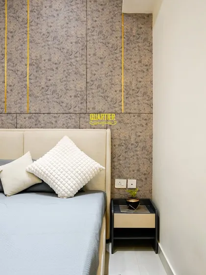A close-up of the bedside area in the Apex D'Rio parents' bedroom. The feature wall combines a subtle textured wallpaper with vertical gold inlay strips, adding a touch of understated luxury.