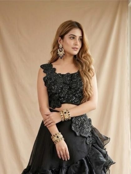A close-up of a modern black Indowestern lehenga. The outfit features a beautifully textured and ruffled skirt paired with a one-shoulder embellished crop top.