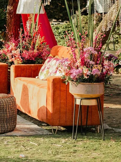 Another view of the outdoor lounge, showing the combination of textures from the velvet sofa to the woven poufs, all surrounded by lush greenery and vibrant flowers.