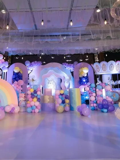 A wide shot of the unicorn party stage, showcasing the various custom props and the colorful balloon decor.