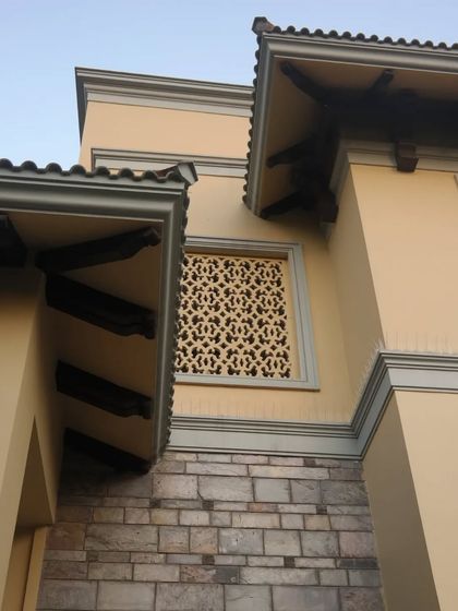 A detail shot looking up at the facade, showing the intricate interplay of the stone-clad base, carved wooden brackets under the eaves, and a decorative trellis window.