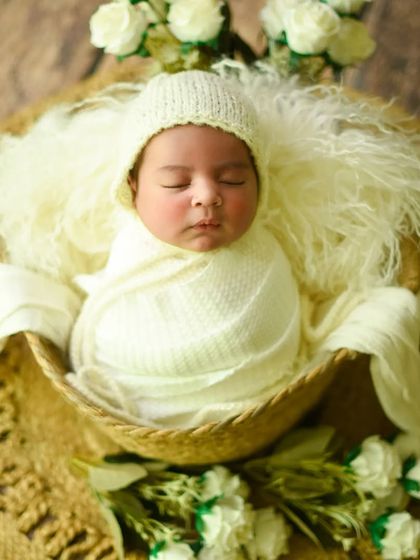 A wider view of the cream-themed setup, with the baby in a basket surrounded by white roses on a jute mat.