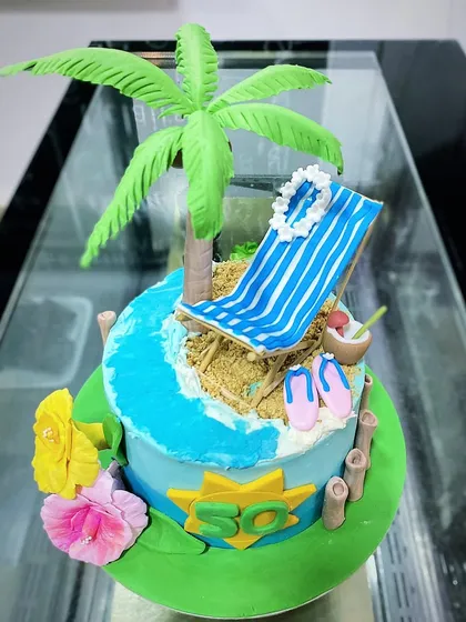 A relaxing beach-themed cake for a 50th birthday. This design features a fondant beach chair, palm tree, and the ocean shore, all completely edible.