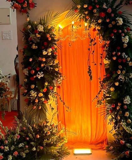 A floral photo booth or entrance decoration for a reception. The warm lighting behind the orange curtain creates a perfect spot for guests to take pictures.