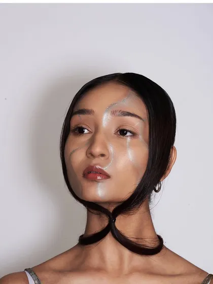 An experimental look combining a glossy, painted face effect with a sculptural hairstyle where the hair is looped to frame the chin.