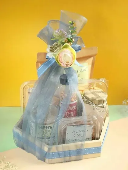 A lovely wooden tray hamper wrapped in soft blue tulle, containing a curated selection of our sweet and savoury items.