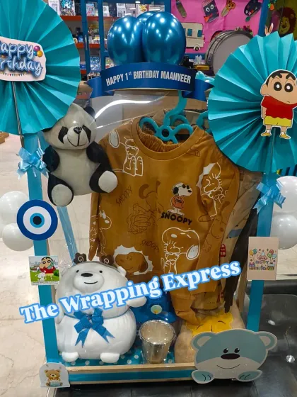 I love creating themed birthday hampers for kids. This one was for a first birthday, featuring a Shinchan and Snoopy theme with clothes, soft toys, and fun decorations, all in a bright blue setup.