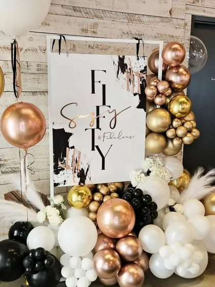 A chic welcome sign for a 50th birthday, framed by a modern balloon arrangement in a sophisticated black, white, and rose gold color scheme.