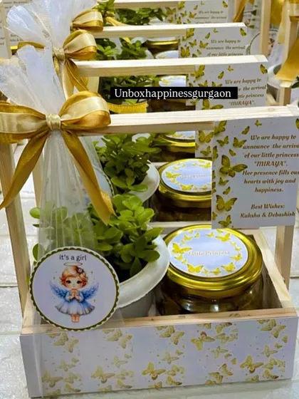 This image focuses on the contents of the announcement basket, including the "It's a girl" tag, a healthy plant, and jars of delicious treats.