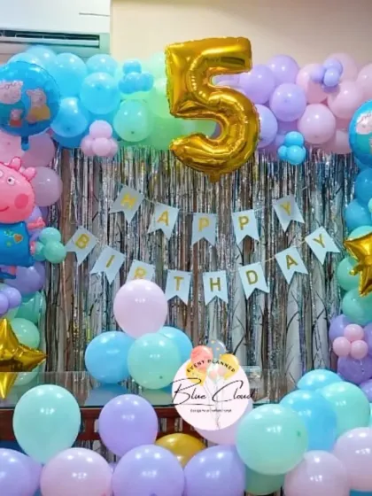 A colorful Peppa Pig birthday setup with a balloon arch over a shimmer curtain, complete with character foils.