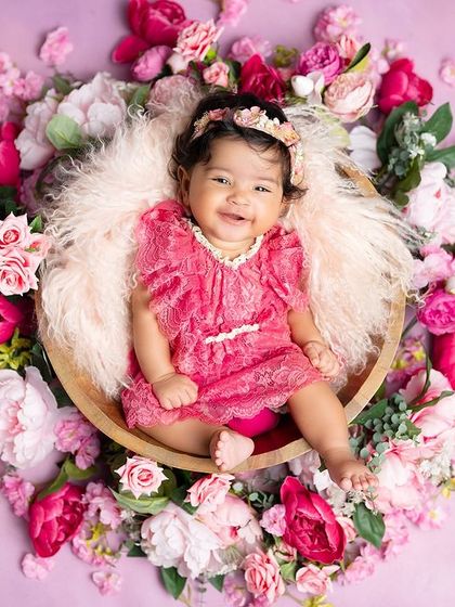 A beautiful, smiling baby girl nestled in a basket of pink flowers. This overhead view creates a stunning and artistic portrait.