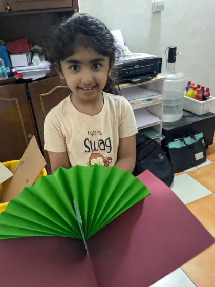 Learning the basics of paper craft. This young student is happy with the fan she created, a simple yet fun exercise in folding and construction.