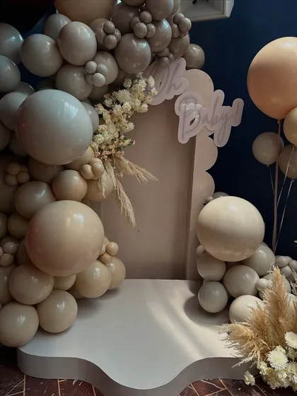 This "Oh Baby" photo backdrop features an organic balloon arch in soft nudes and beiges, accented with dried pampas grass for a touch of bohemian chic.