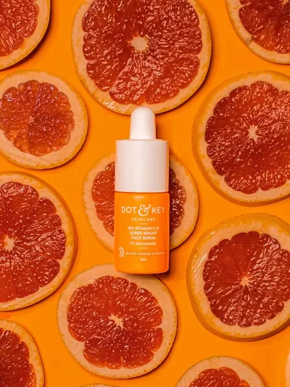 A vitamin C serum surrounded by slices of fresh grapefruit on a vibrant orange background. This flat-lay shot directly communicates the product's key ingredient and its zesty, energizing properties.