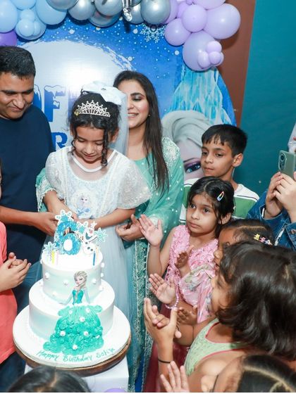 The grand cake-cutting moment at the Frozen party, with the birthday girl surrounded by her friends and family, all singing for her.