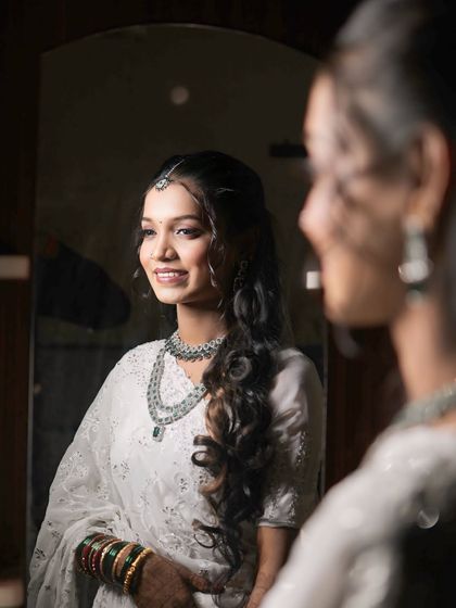 A beautiful shot of a Buddhist bride looking in the mirror. Her hair is styled with long, soft curls, creating a romantic and ethereal look.