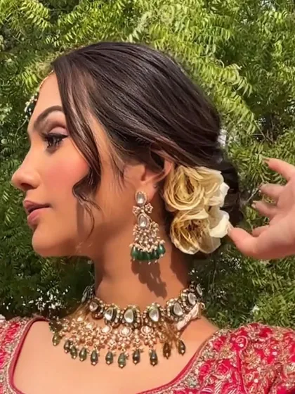 A soft and romantic messy bun with beautiful white and gold roses. The loose tendrils frame the face, creating an effortlessly chic bridal look.