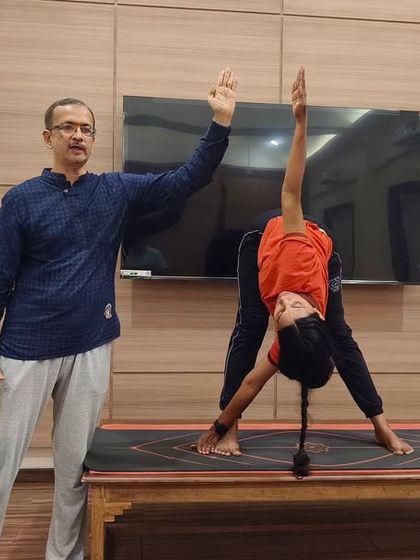 An instructor demonstrates the correct form for Trikonasana (Triangle Pose) to a student. This one-on-one guidance is integral to our teaching philosophy, ensuring postures are learned with precision.