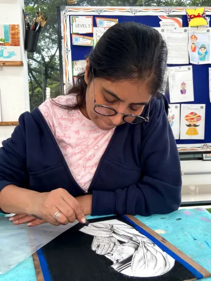 A student works on a reverse drawing, using an eraser to create highlights on a charcoal-covered surface.