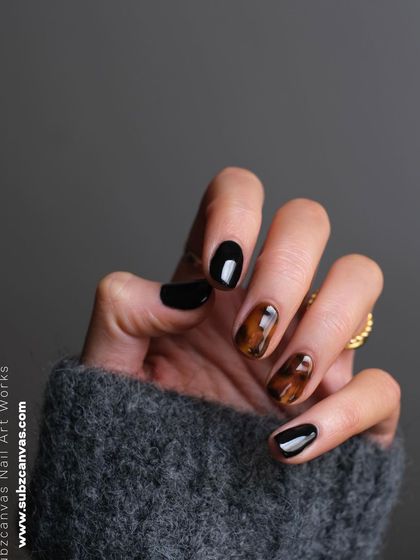 A chic and sophisticated tortoiseshell nail art design. This effect is created by layering sheer brown and black polishes, perfectly complemented by solid black nails for a timeless look.